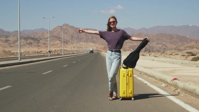 Young handsome female traveler with ukulele and yellow luggage hitchhiking 4k