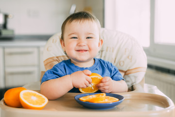 little girl sitting in baby chair, eating an orange