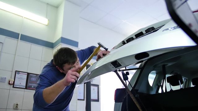 Paintless Dent Repair. A man in a blue pullover repairs the trunk at a car repair shop. Repair of dents without painting, tools, hammer, master class