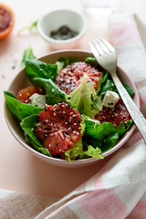 Spring fresh salad with blood orange, lettuce, spinach and sesame seeds on pink background. Top view. Selective focus