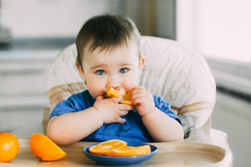 little girl sitting in baby chair, eating an orange