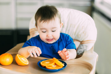 little girl sitting in baby chair, eating an orange