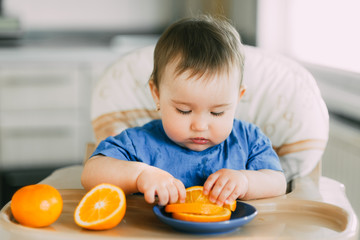 little girl sitting in baby chair, eating an orange