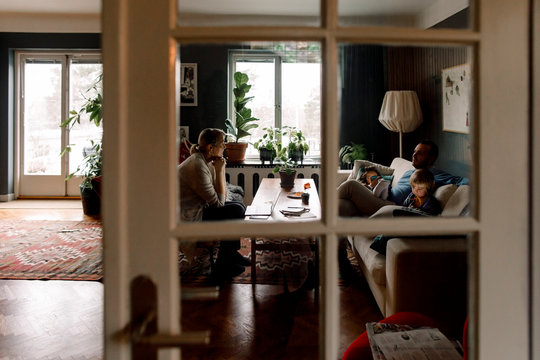 Family using various technologies in living room seen through transparent door at home