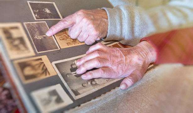 Elderly couple hands looking at old pictures album at home. Detail on hands and old images