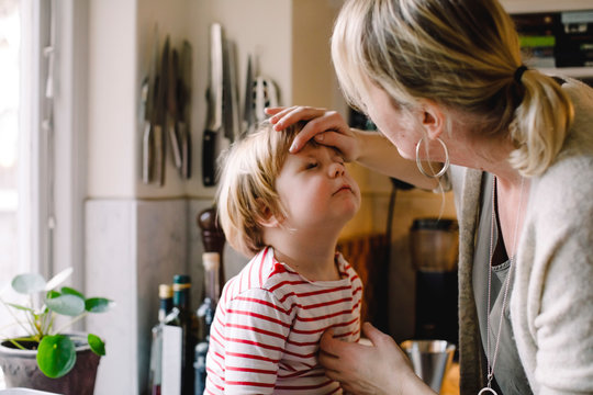Caring mother looking at daughter's bruised eye in kitchen