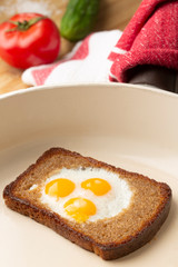Scrambled quail eggs on rye bread in a pan with tomato and cucumber for breakfast. Toasted bread with fried egg and fresh vegetables.