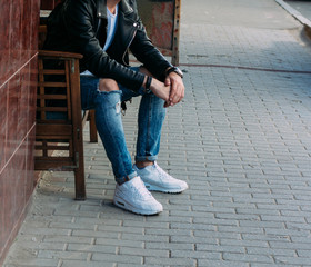 attractive guy sitting on a bench in a cafe, on the street, white sneakers, white T-shirt, black leather jacket and black jeans, pants. model. waiting for a meeting.