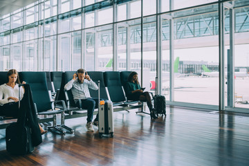 Full length of multi-ethnic colleagues waiting while sitting at airport departure area