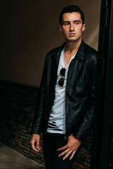 Obraz premium young, handsome guy in a white T-shirt, black, leather jacket and black pants is on the street, on the T-shirt sunglasses. model, city walk, live style