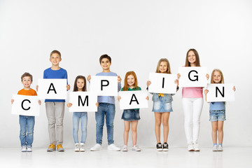 Campaign. Group of happy smiling children and teenagers or young team with a white banners holding word isolated in light studio background. Education and advertising concept.
