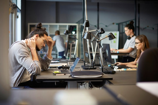Tensed male entrepreneur looking at laptop while sitting in creative office