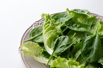 A mixture of spinach leaves and salana leaves on a plate. Selective focus, white background.
