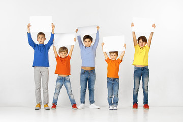 Group of angry children with a white empty banners isolated in studio background. Education and advertising concept. Protest and children's rights concepts.