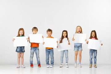 Group of angry children with a white empty banners isolated in white studio background. Education and advertising concept. Protest and children's rights concepts.