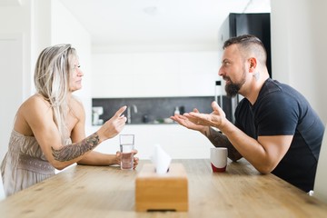 Man and woman sitting by table on opposite side and arguing problems