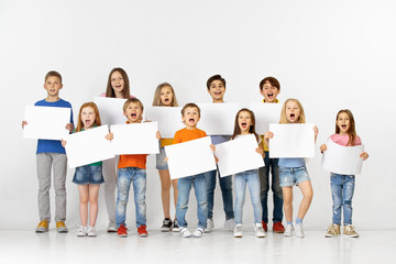 Obraz premium Grupa szczęśliwych dzieci krzyczących z białymi pustymi bannerami na białym tle w świetle studia tło. Koncepcja edukacji i reklamy