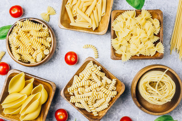 Various pasta on wooden bowls over light gray background