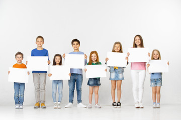 Obraz premium Group of happy smiling children with a empty banners isolated in light studio background. Education and advertising concept
