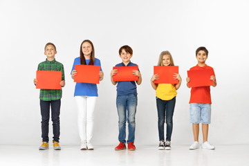 Obraz premium Group of happy smiling children with red empty banners isolated in white studio background. Education and advertising concept