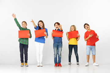 Obraz premium Group of happy smiling children with red empty banners isolated in white studio background. Education and advertising concept