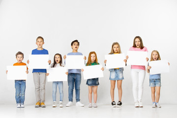 Obraz premium Group of happy surprised children with a white empty banners isolated in white studio background. Education and advertising concept