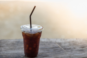 Close up of plastic take away cup of iced black coffee americano  on wooden table with copy space.