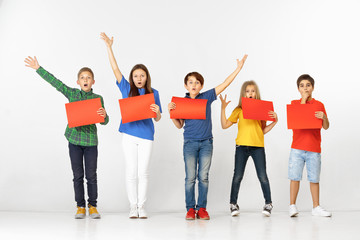 Fototapeta premium Group of happy surprised children with red empty banners isolated in white studio background. Education and advertising concept