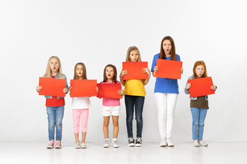 Fototapeta premium Group of happy surprised children with red empty banners isolated in white studio background. Education and advertising concept
