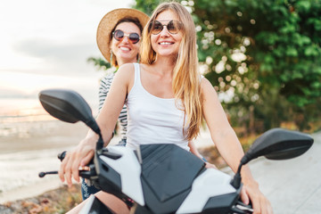 Two laughing girlfreinds motorbike travelers portrait behind the sunset sea coas