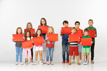 Fototapeta premium Group of sad serious angry children with red empty banners isolated on studio background. Education and advertising concept. Protest and children's rights concepts.