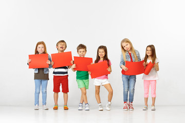 Group of unhappy sad children with red empty banners isolated in white studio background. Education and advertising concept. Protest and children's rights concepts.