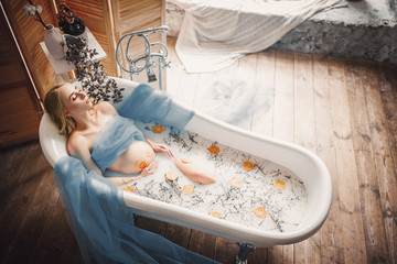 Pregnant woman takes a bath with milk, lavender herbs and orange slices.