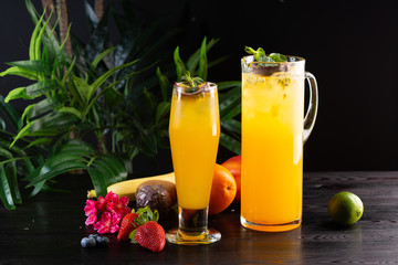 Mango lemonade - passion fruit in a jug and a glass and fruit on a dark wooden background