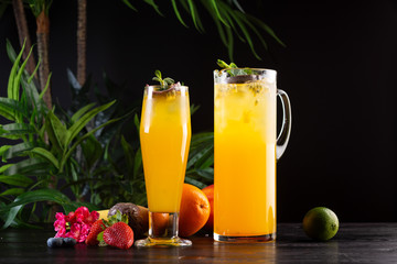 Mango lemonade - passion fruit in a jug and a glass and fruit on a dark wooden background