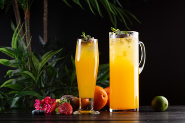 Mango lemonade - passion fruit in a jug and a glass and fruit on a dark wooden background