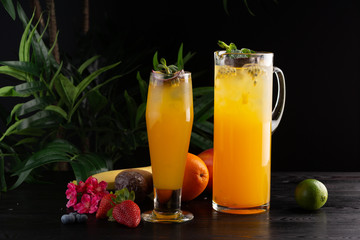 Mango lemonade - passion fruit in a jug and a glass and fruit on a dark wooden background