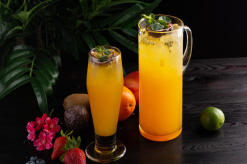 Mango lemonade - passion fruit in a jug and a glass and fruit on a dark wooden background