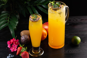 Mango lemonade - passion fruit in a jug and a glass and fruit on a dark wooden background