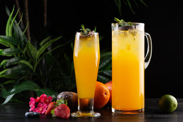 Mango lemonade - passion fruit in a jug and a glass and fruit on a dark wooden background