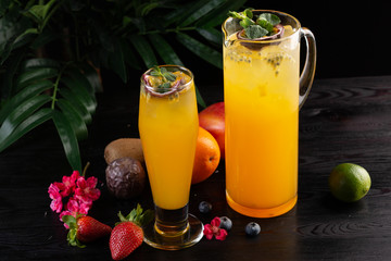 Mango lemonade - passion fruit in a jug and a glass and fruit on a dark wooden background