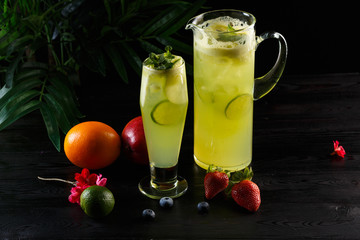 Green apple lemonade with lime in a jug and glass and fruits on a dark wooden background