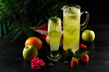 Green apple lemonade with lime in a jug and glass and fruits on a dark wooden background