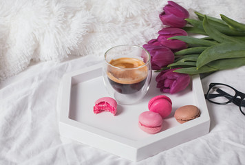 Fototapeta na wymiar A cup of coffee, macarons and tulips on the white bedsheets.