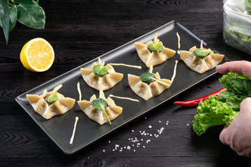 Gyoza with spinach, ricotta and lamb on a black rectangular plate on a dark wooden background
