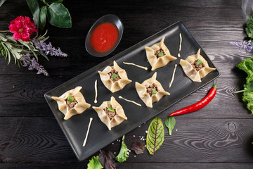 Gyoza with spinach, ricotta and lamb on a black rectangular plate on a dark wooden background