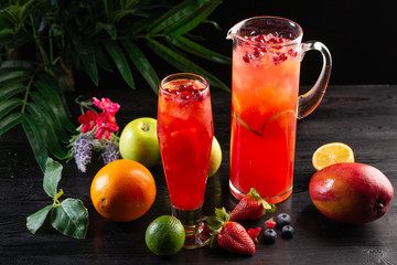 Cranberry lemonade - lingonberries in a jug and glass and fruits on a dark wooden background