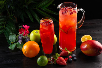 Cranberry lemonade - lingonberries in a jug and glass and fruits on a dark wooden background