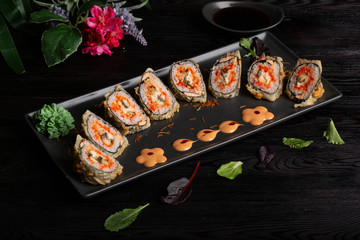 Set sushi rolls on a black rectangular plate on a dark wooden background
