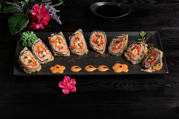 Set sushi rolls on a black rectangular plate on a dark wooden background